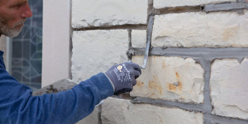 Professional mason performing precise tuckpointing technique on a stone wall.