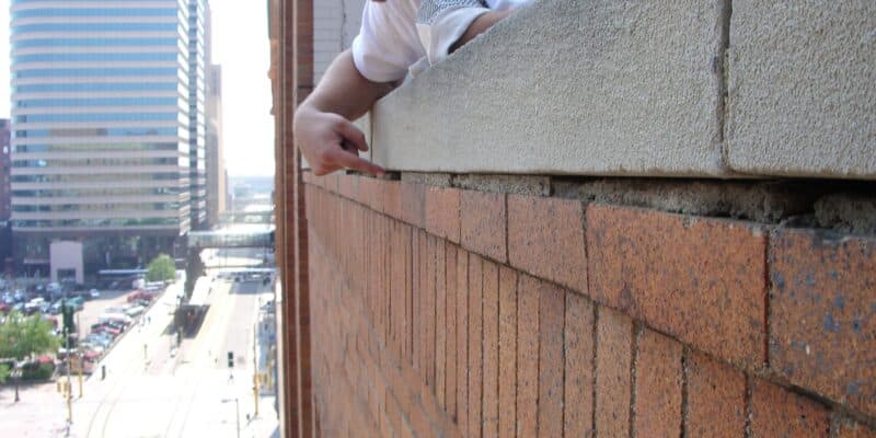 BRC tech inspecting deteriorated mortar joints on brick facade.